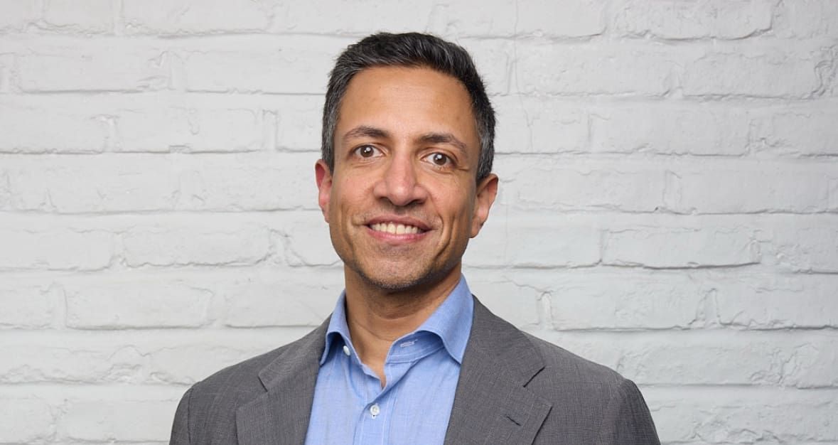 A man in a suit and blue shirt smiling.